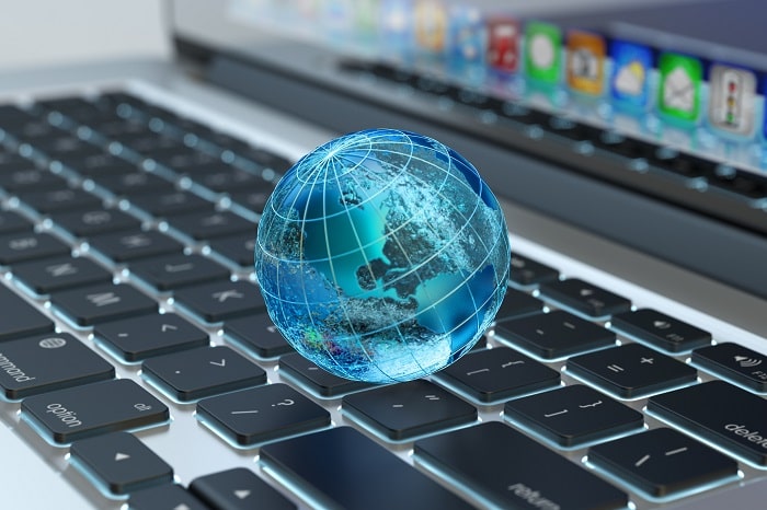 The picture illustrates a small earth globe in blue color placed on the keyboard of a laptop.